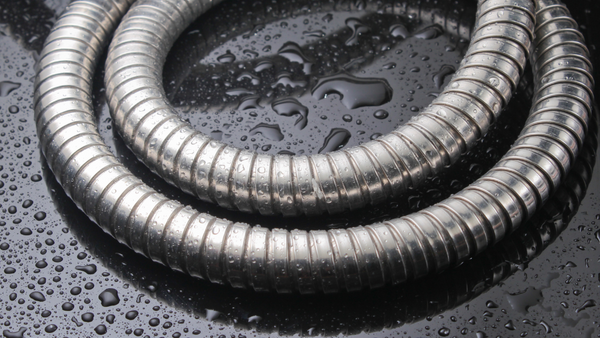 An all metal shower hose is pictured on a black background with water droplets