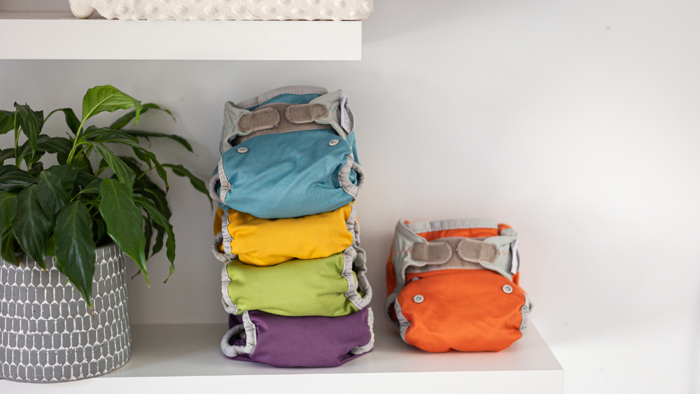 Multicolored cloth diapers are stacked up on a white table after being cleaned with a cloth diaper sprayer.