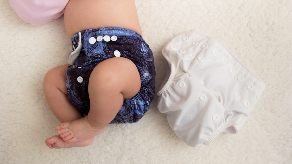 A baby's body and legs are shown wearing a cloth diaper, which has been cleaned with a cloth diaper sprayer