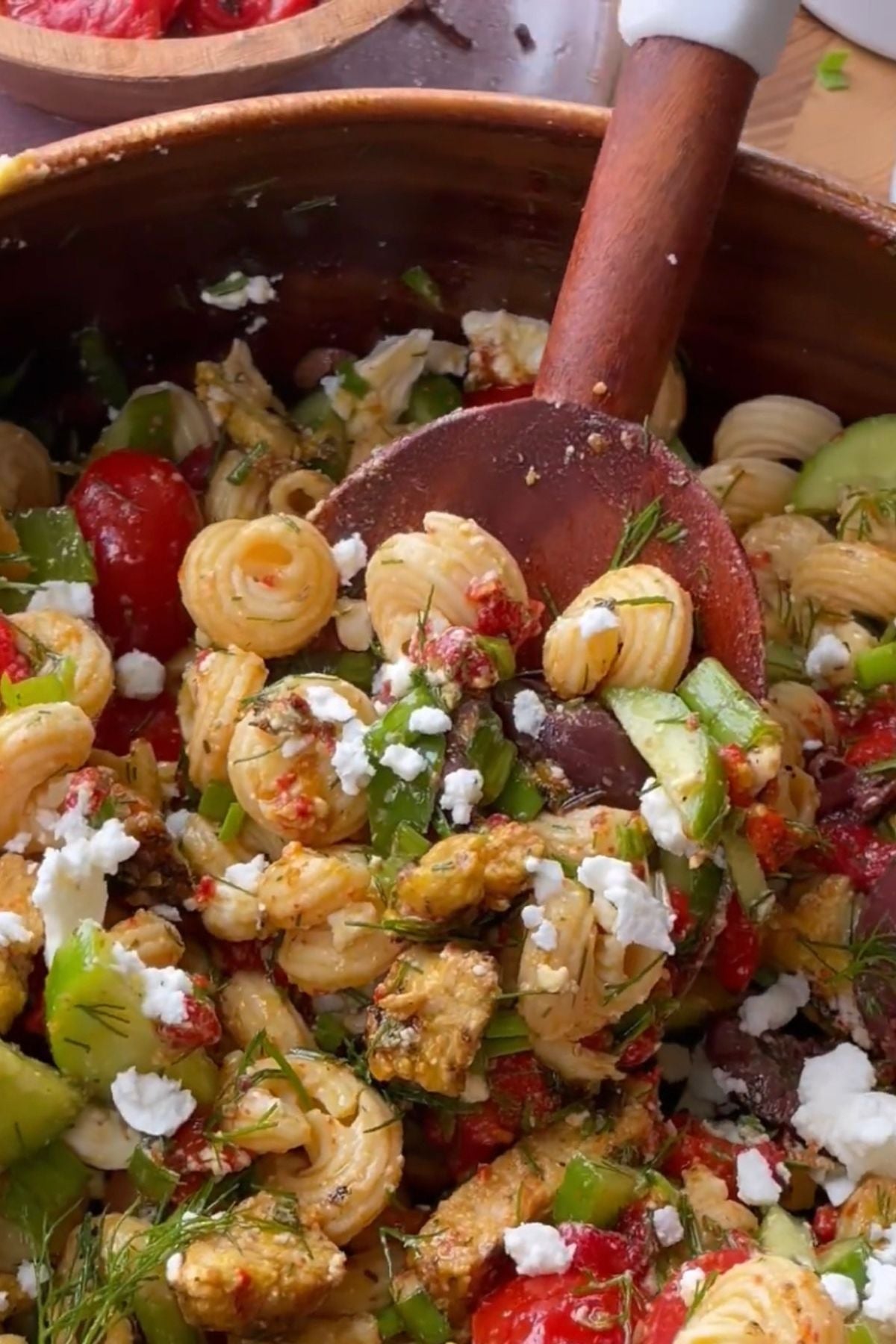 mediterranean pasta salad in a bowl with a wooden spoon.