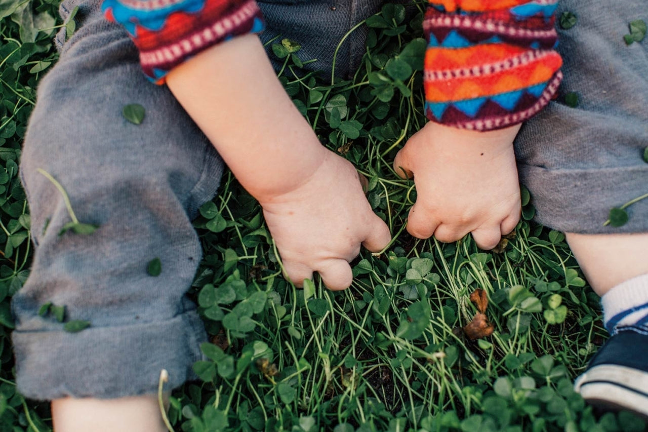 Toddler sitting on grass, hands clawing at cloves. Photo: Kyle Sparks