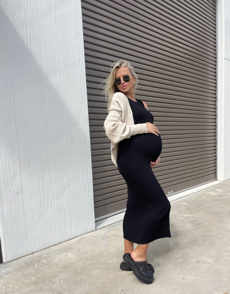 Pregnant Woman wears a Cropped Cardigan (Light Sand) over a Black Maternity Dress