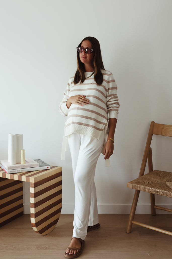 Pregnant woman wearing striped maternity jumper over white maternity pants.