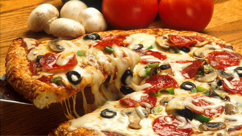 Vegetarian pizza in foreground with tomatoes and mushrooms in background