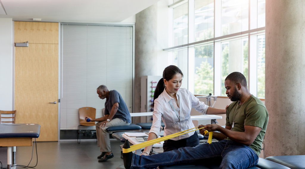 A woman helping a male patient perform physical therapy exercises with resistance bands.