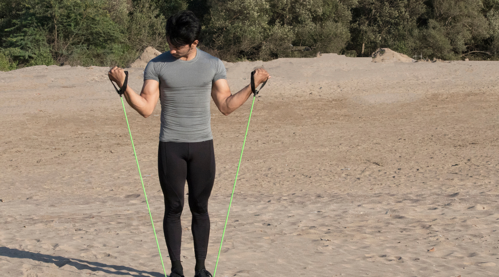 A man doing standing bicep curls on the beach.