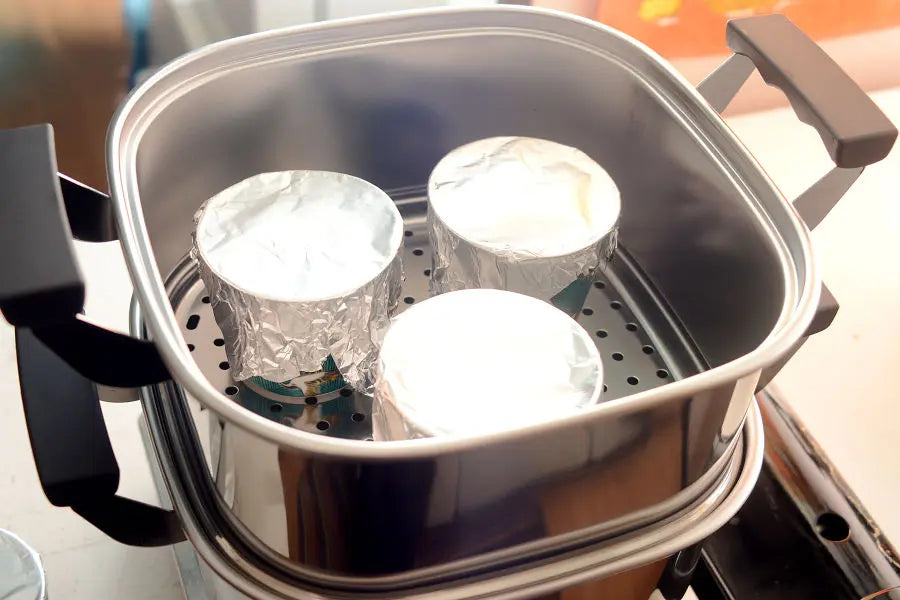 When the water has started boiling, place the teacups covered with aluminum foil on the top layers of the steamer.