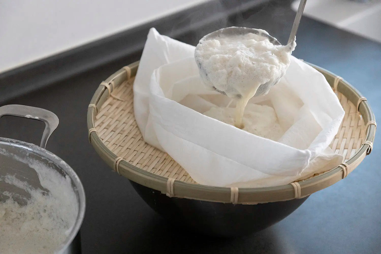 Pouring soybean smoothie into cheesecloth and draining into bowl