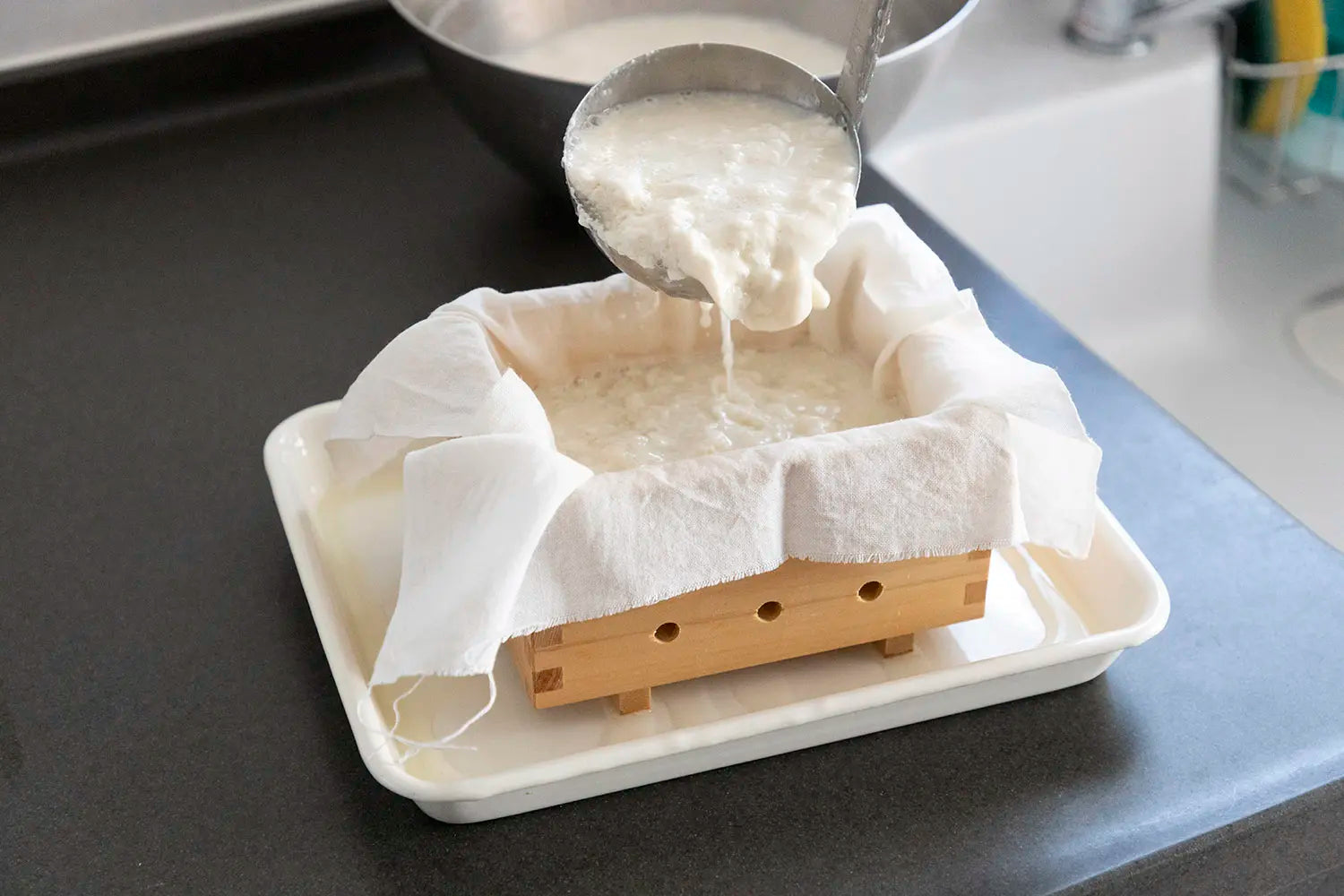 Pouring tofu curds into wooden tofu maker