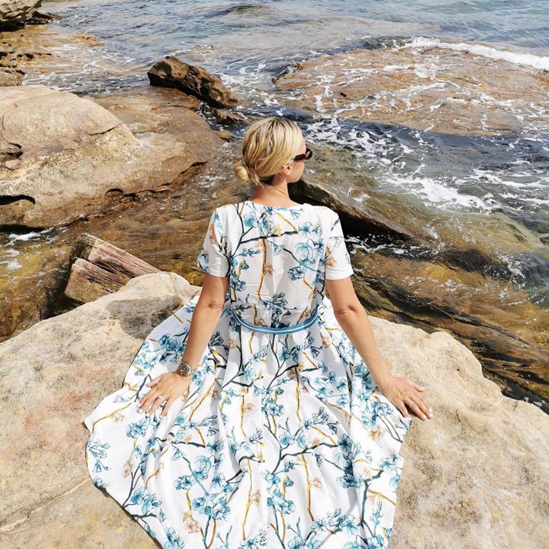 Model blogger Nikki Phillips sits on rock wearing floral resort dress by Robe luxury resort wear