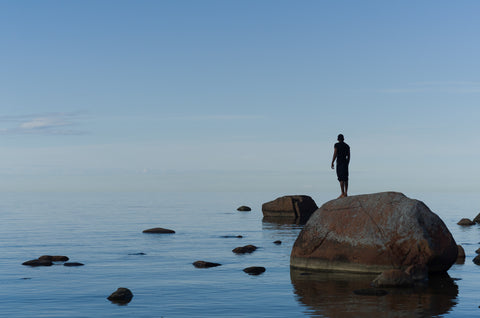 A man by the ocean, standing on a rock.