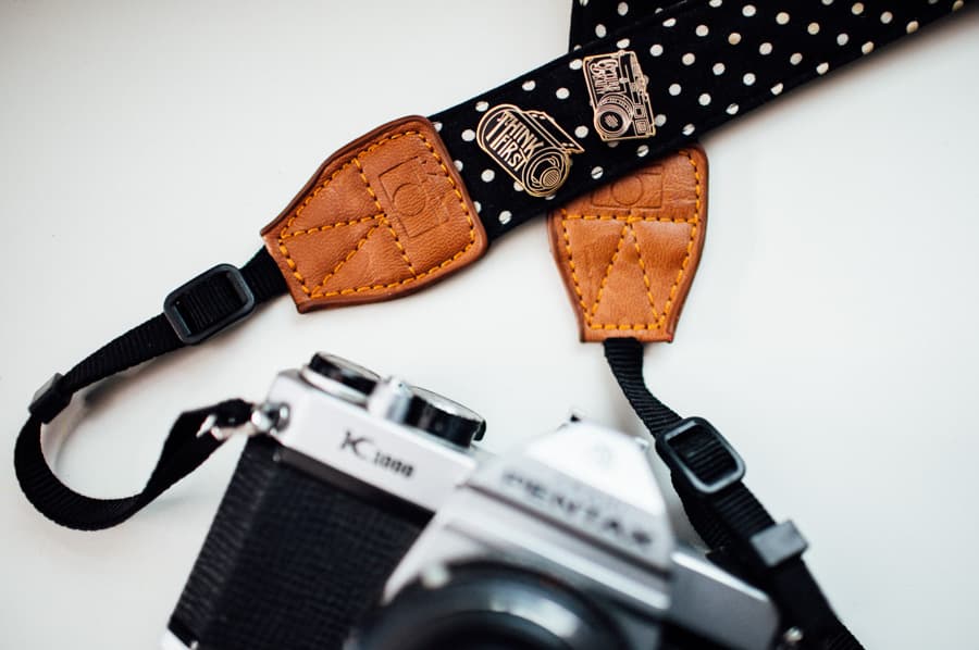 Camera strap with enamel pins attached