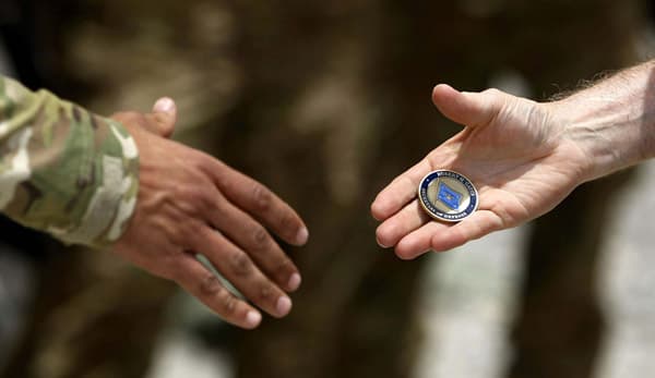 Two people shaking hands passing a challenge coin between them