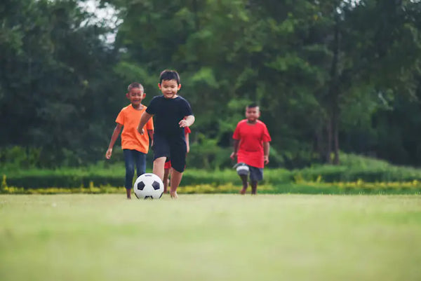 anak anak sedang bermain sepak bola di tengah lapangan hijau