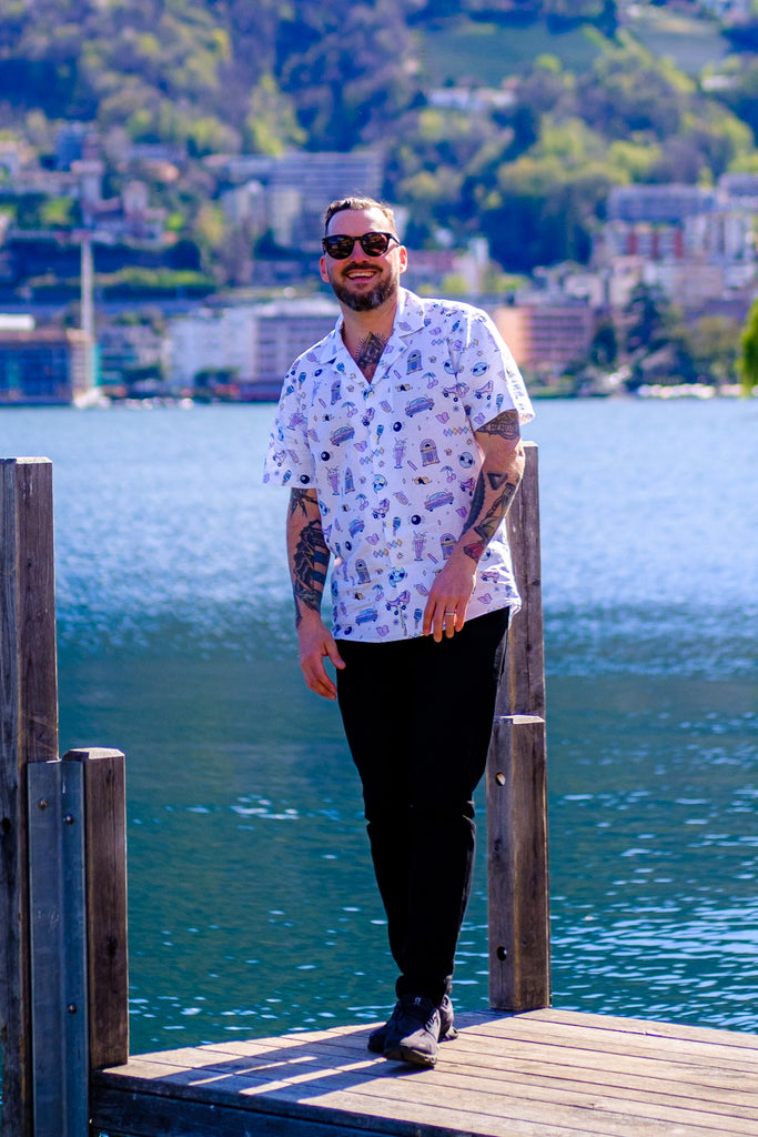 A promotional image of a shirt with a vintage 50s-inspired print on a white background. The shirt is made from a breathable blend of 53% linen and 47% cotton fabric and is shown hanging on a hanger. The text reads "Introducing our latest summer shirt - a total ode to the 50s. The print features elements and colors that will transport you back to the golden era.