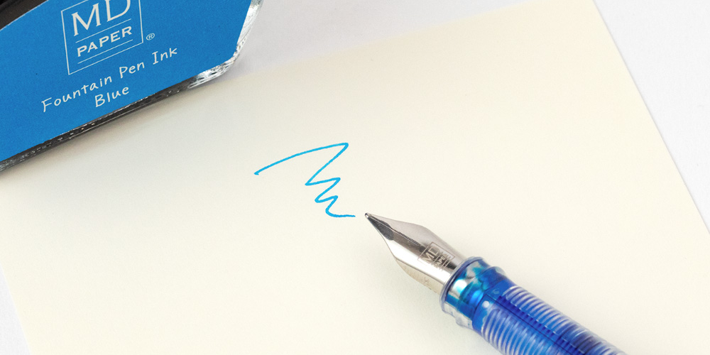 A picture of a fountain pen leaving a blue line on paper next to a blue ink bottle