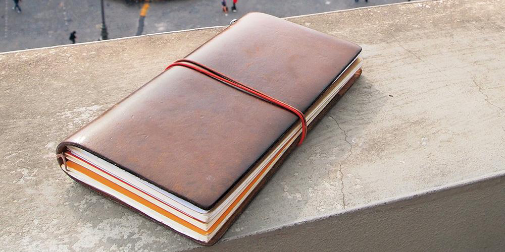 A brown leather Traveler's Notebook regular size sitting on a balcony edge from a height