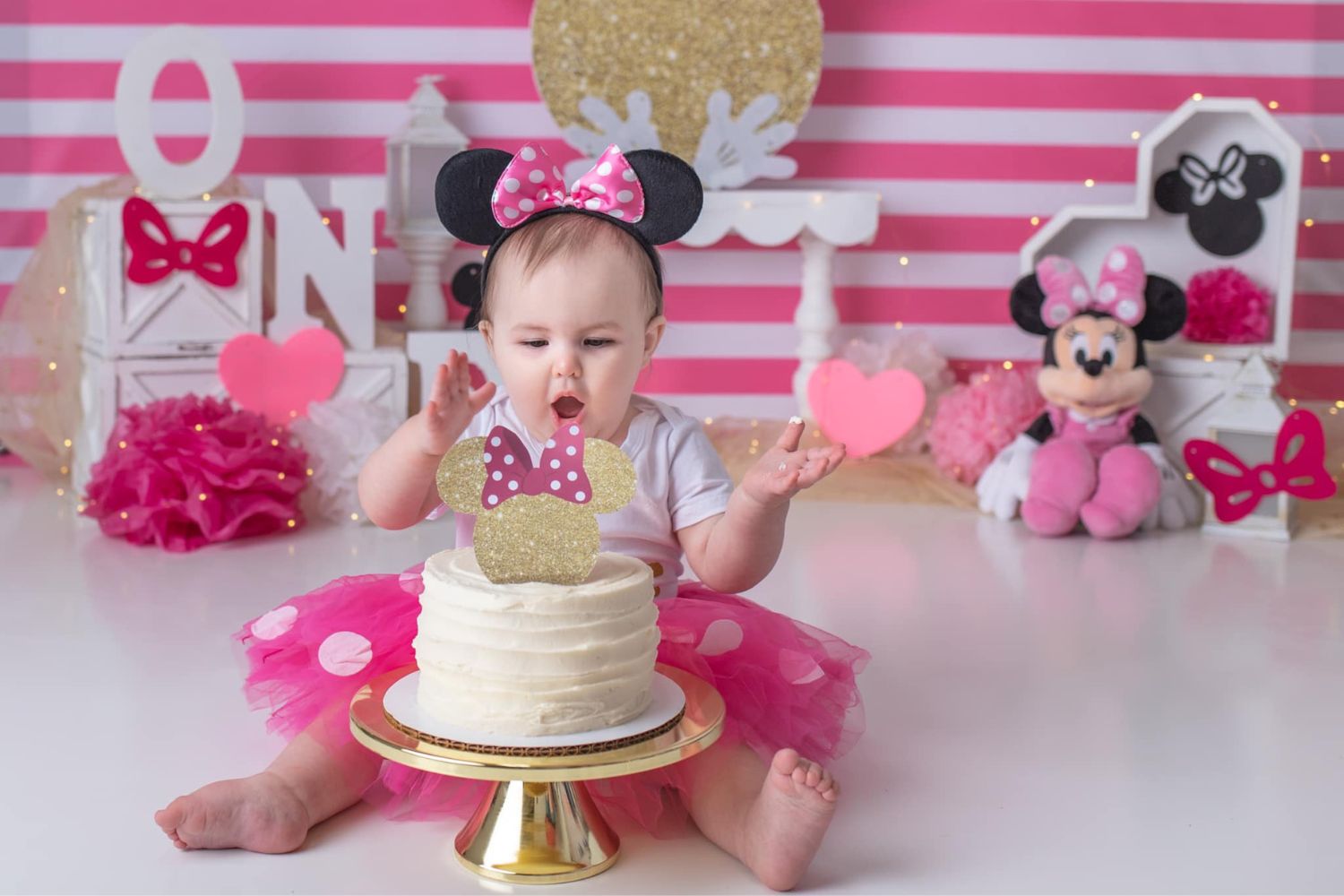 baby girl's playing with her birthday cake in front of a pink and white stripe