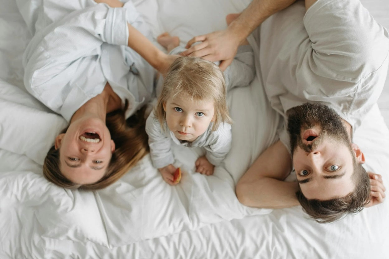 A family of three lying in bed looking at the camera