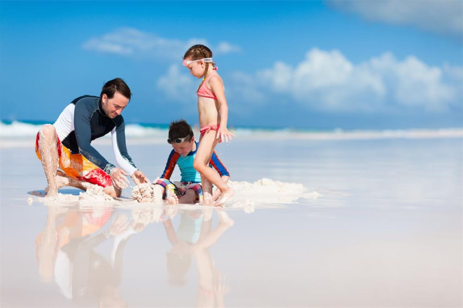 dad playing sand with his boy and girl on beach