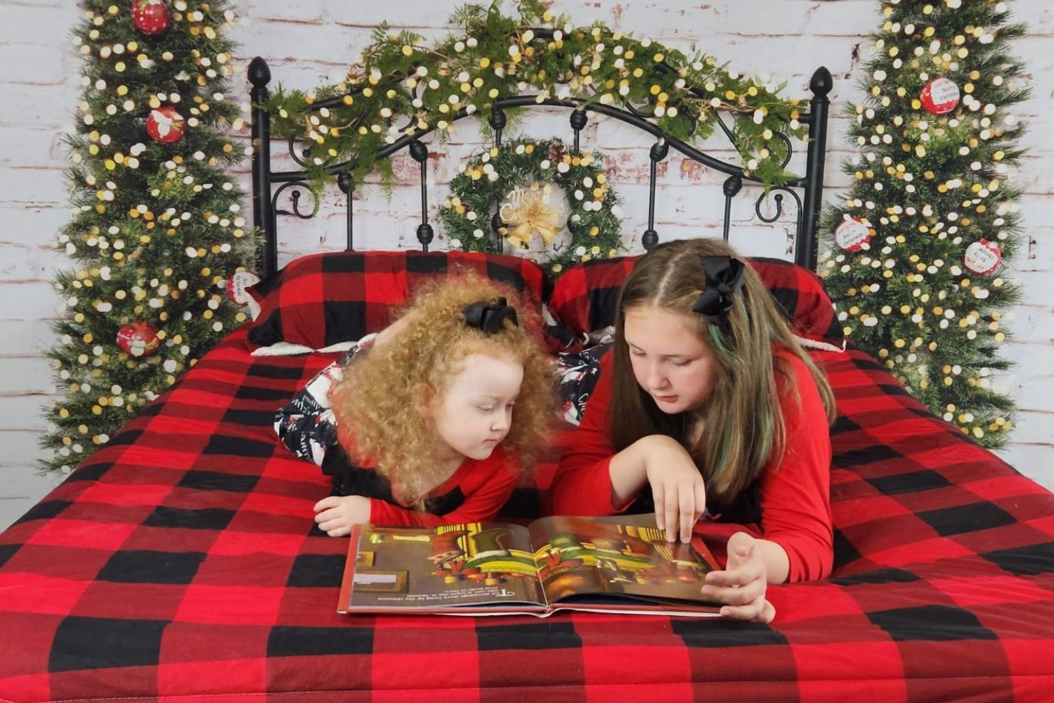 two girls reading book on Christmas decorated bed