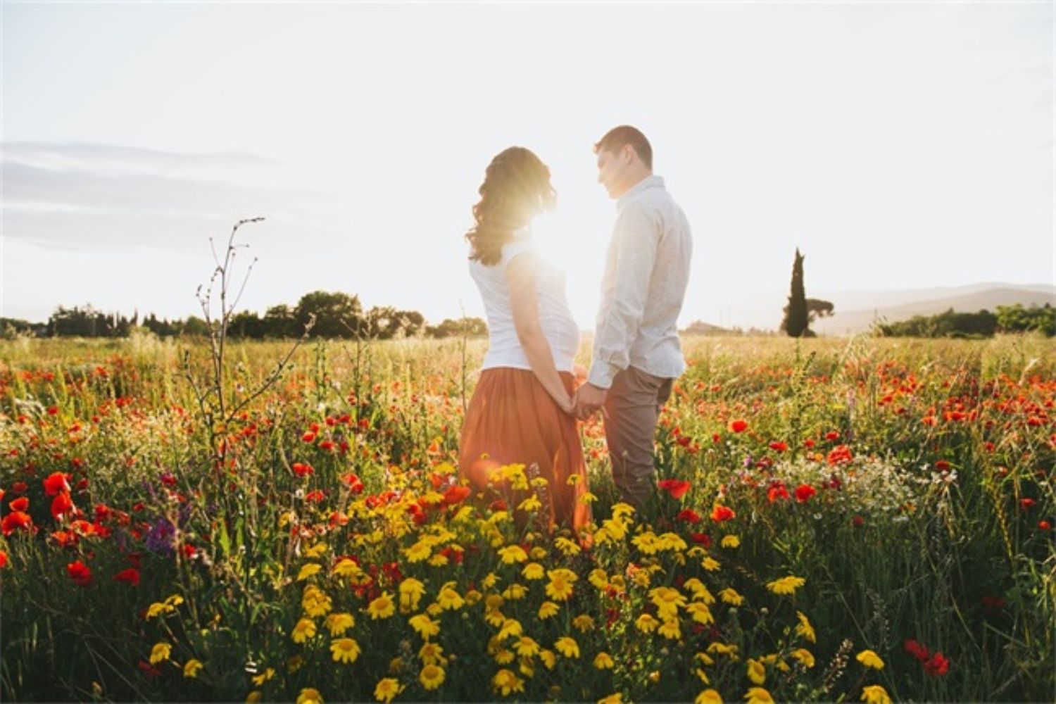 couple maternity photo by standing in the field of flowers
