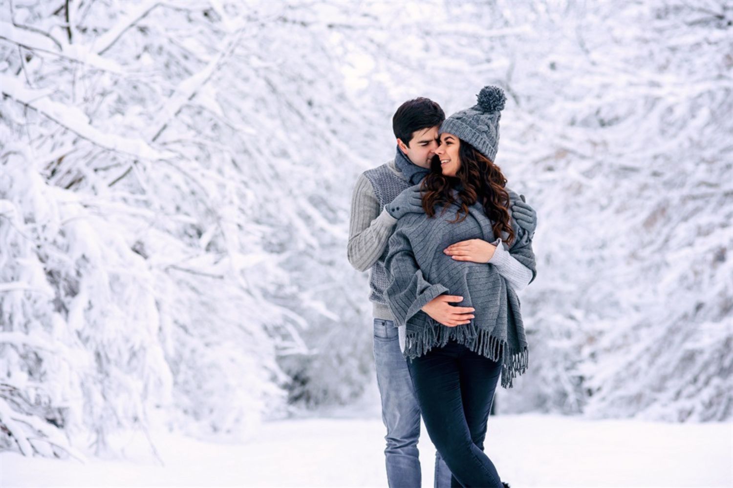 couple maternity photo by standing and holding each other in the snow