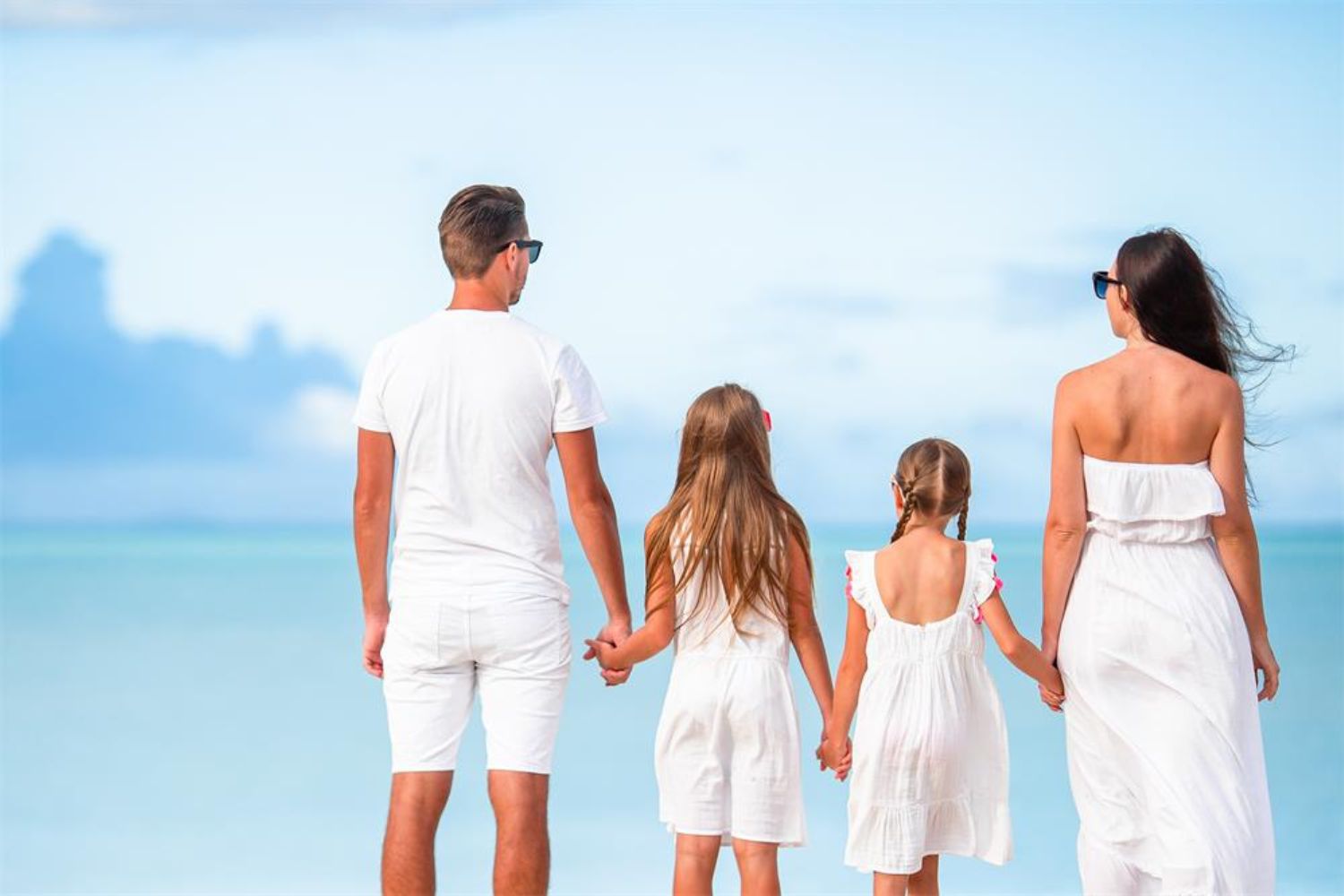 family holding hands standing on beach in all white