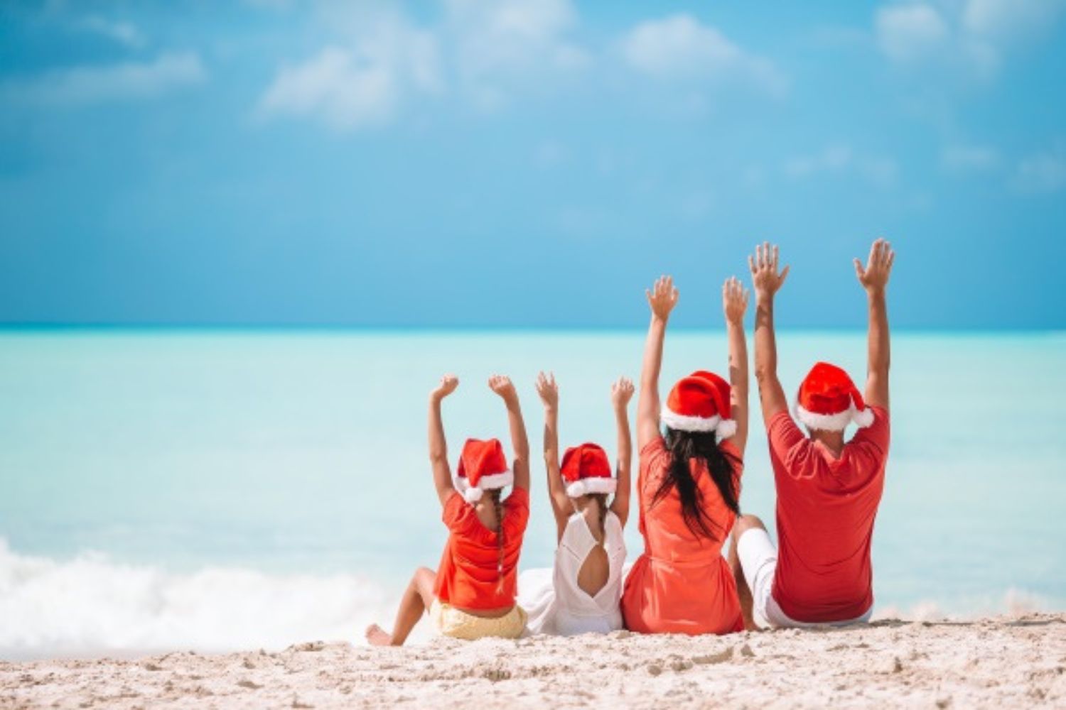 family sitting and puting hands up at the beach with Santa hats