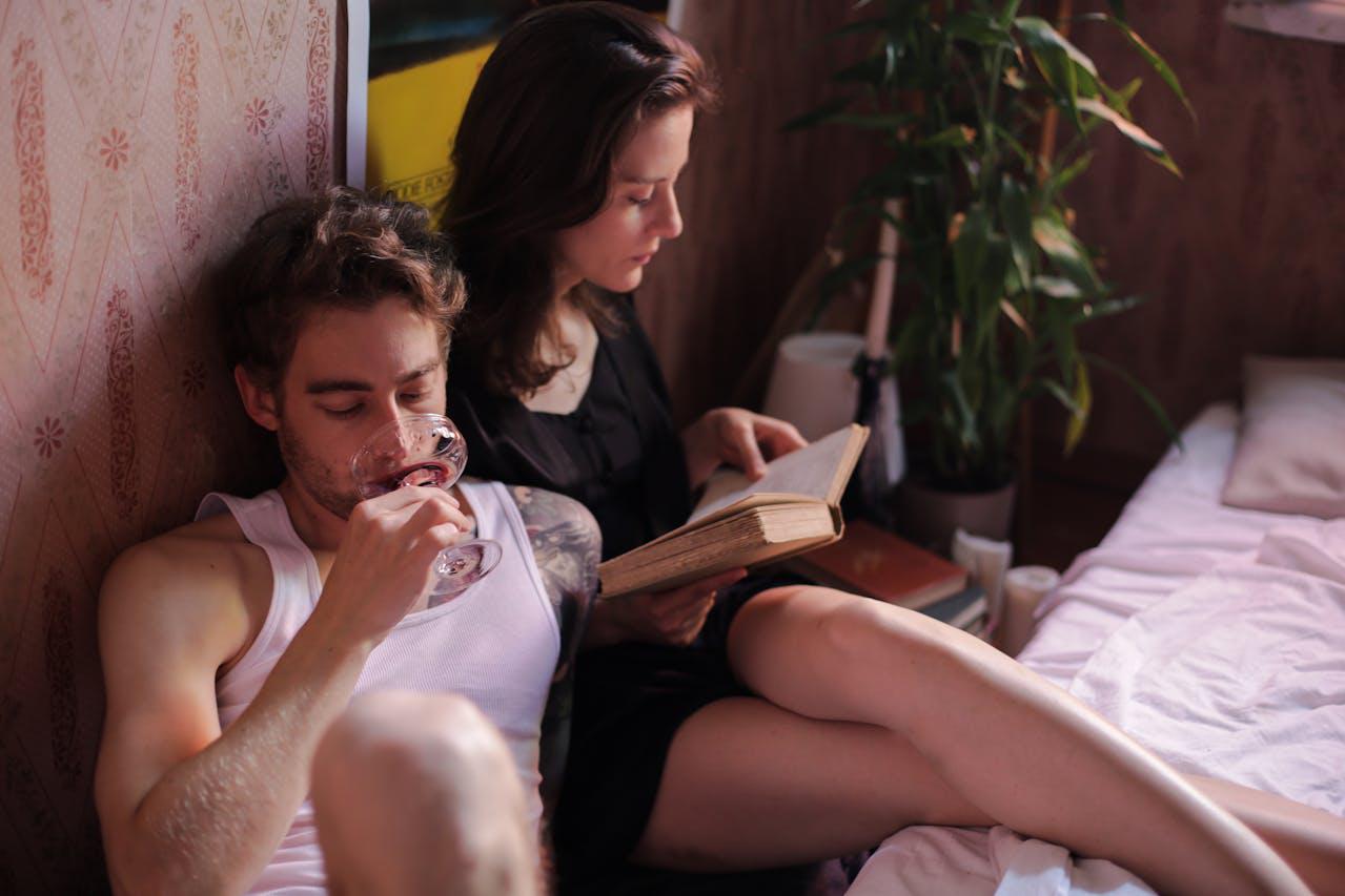 A couple relaxing at home, with one reading a book and the other sipping wine.