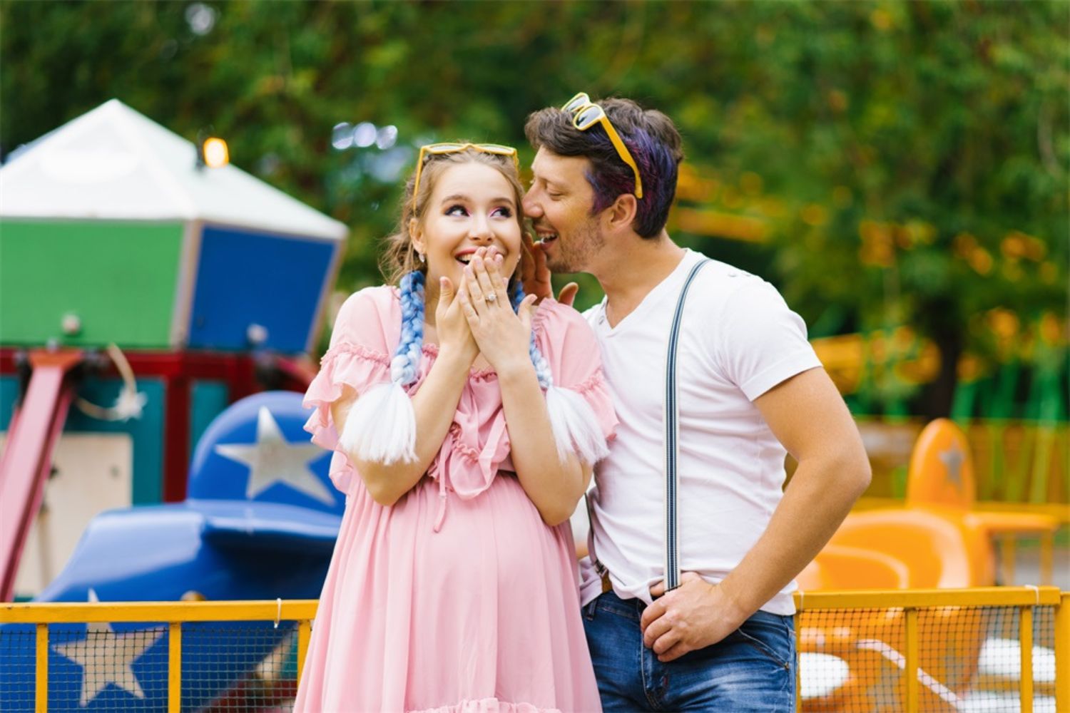 couple maternity photo of wispering in a amusement park