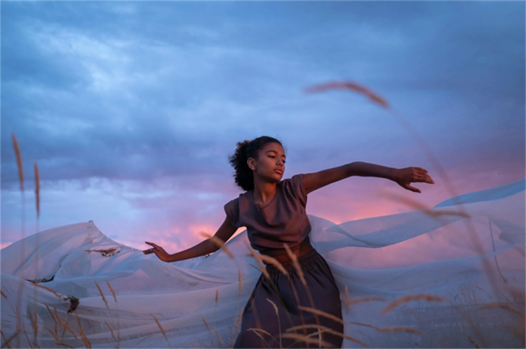 Woman dancing in a field at sunset with flowing fabric.