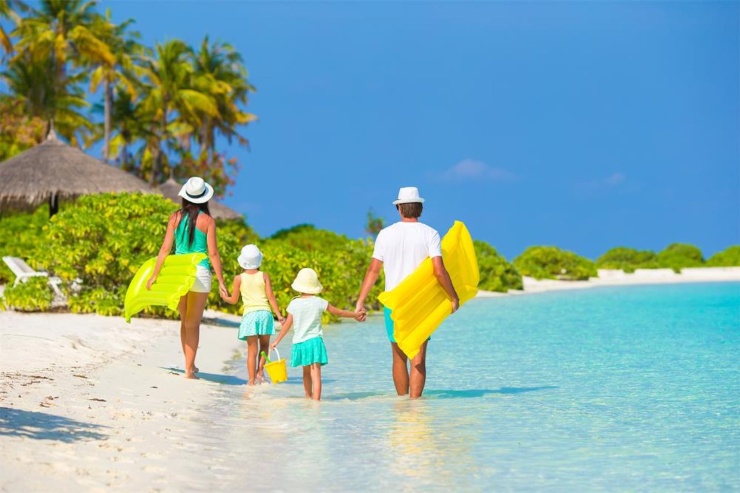 family walking on beach and holding yellow floating cushion