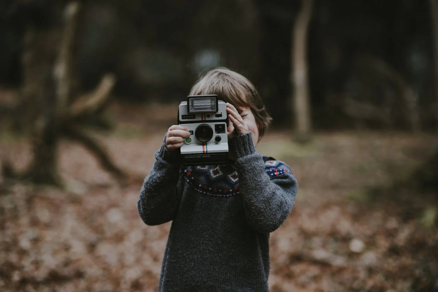 a little boy taking photo with polaroid camera in the forest
