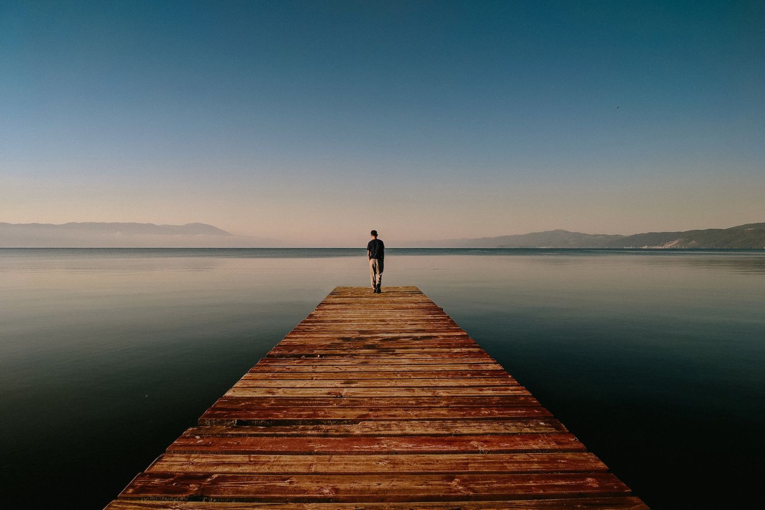 man standing on the pier edge over lake