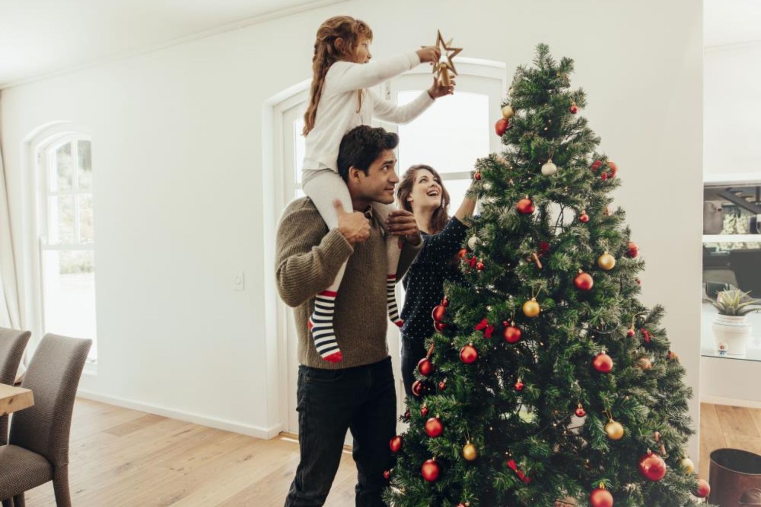 little girl putting the high star on the Christmas tree on her father's shoulder