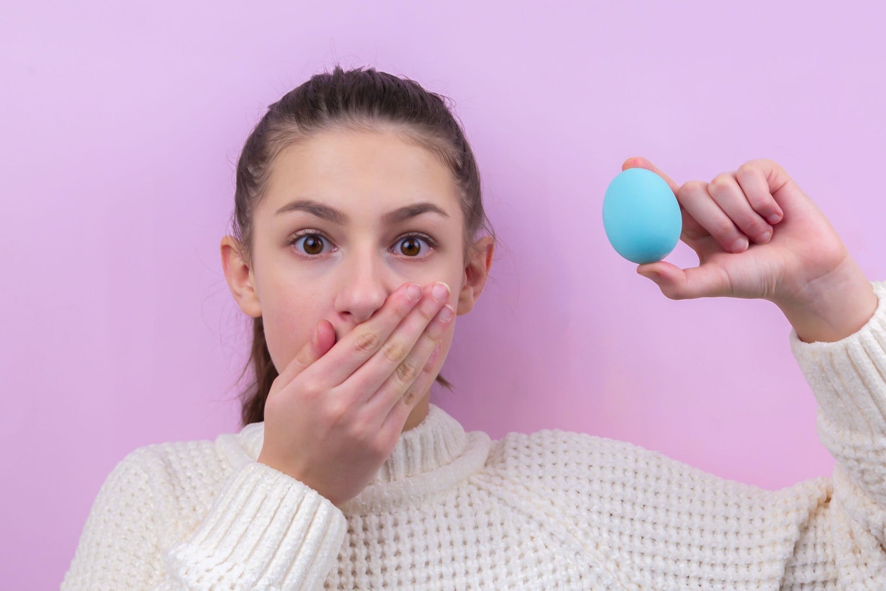 a photo of a girl holding an Easter egg in one hand and the othre coving her mouth