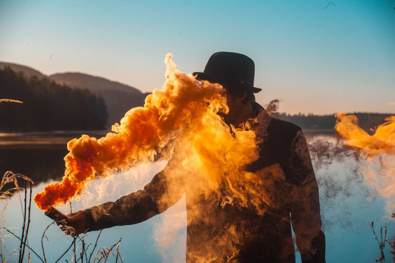 a man holding bomb smoke in front of a lake 