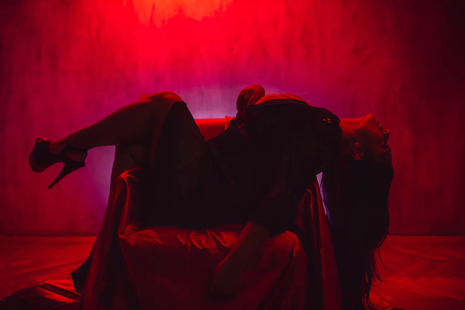 A plus-size woman is lying on a chair with her head thrown backward and her heels showing off in red lights.