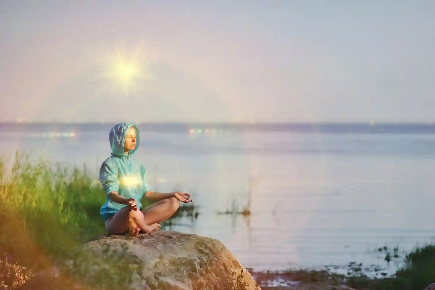 Meditating woman with aura colors in yoga position on a stone near the lake