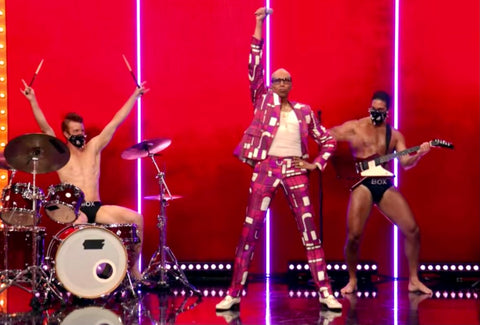 RuPaul dances on stage with box boys playing instruments 
