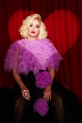 Katy Perry in pink dress with blond hair with  red curtain behind and hear shaped light