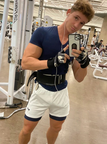 Model flexes in gym selfie in white shorts blue v necl