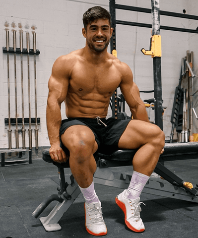 Dan Tai sat on a gym bench shirtless, showing his huge legs and smiling. 