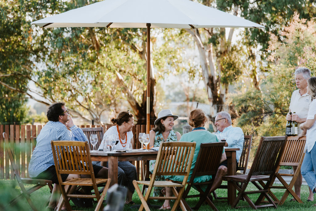 Group of adults sitting at outdoor table talking and enjoying wine