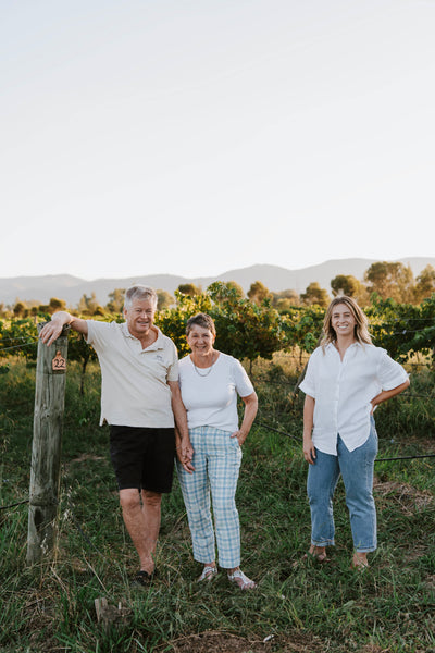 Owners of Vinifera Wines Tony, Debbie and Sam standing in front of the vineyard with the hills beyond