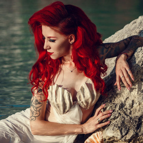Woman with long red hair sitting in the ocean.