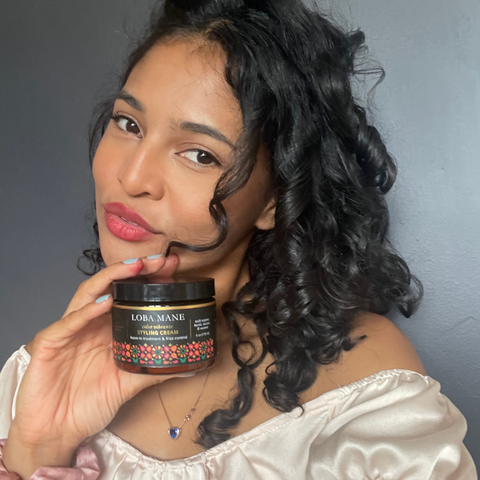 Woman with defined curls and bold lipstick, holding Loba Mane's Styling Cream and smiling.