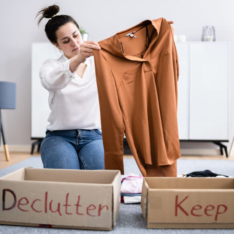 Woman holding an orange sweater and deciding if it should go into a "declutter" box or a "keep" box.