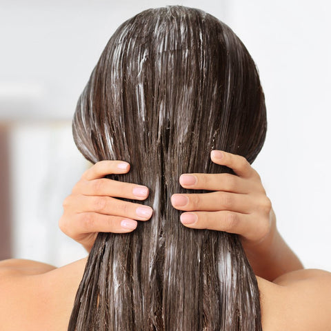 Person with a hair mask in their hair, touching the back of their head.